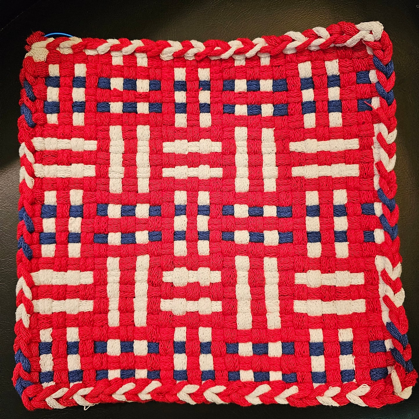 Woven trivet with red, white, and blue pattern on a dark background