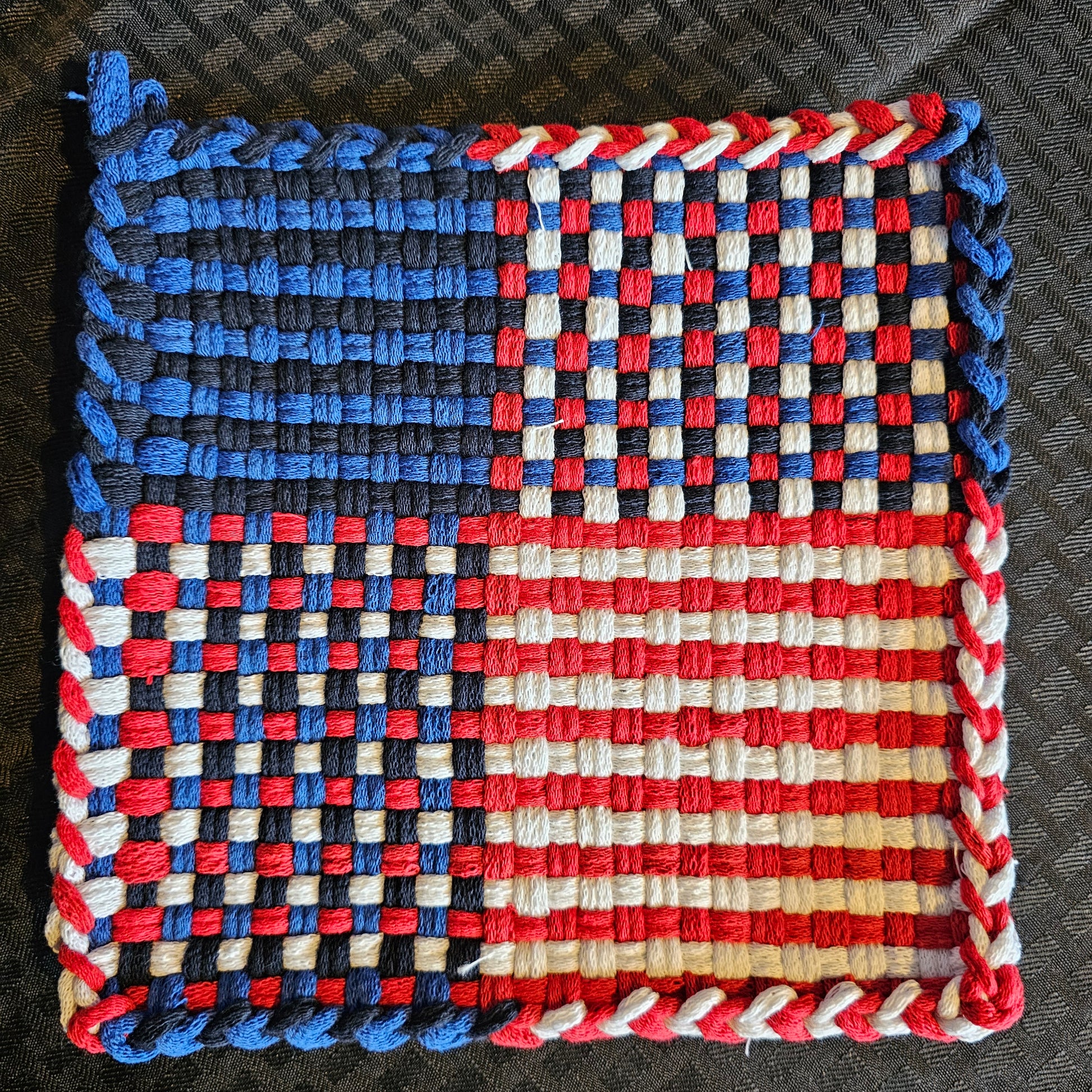 Woven trivet with red, white, and blue pattern on a dark background