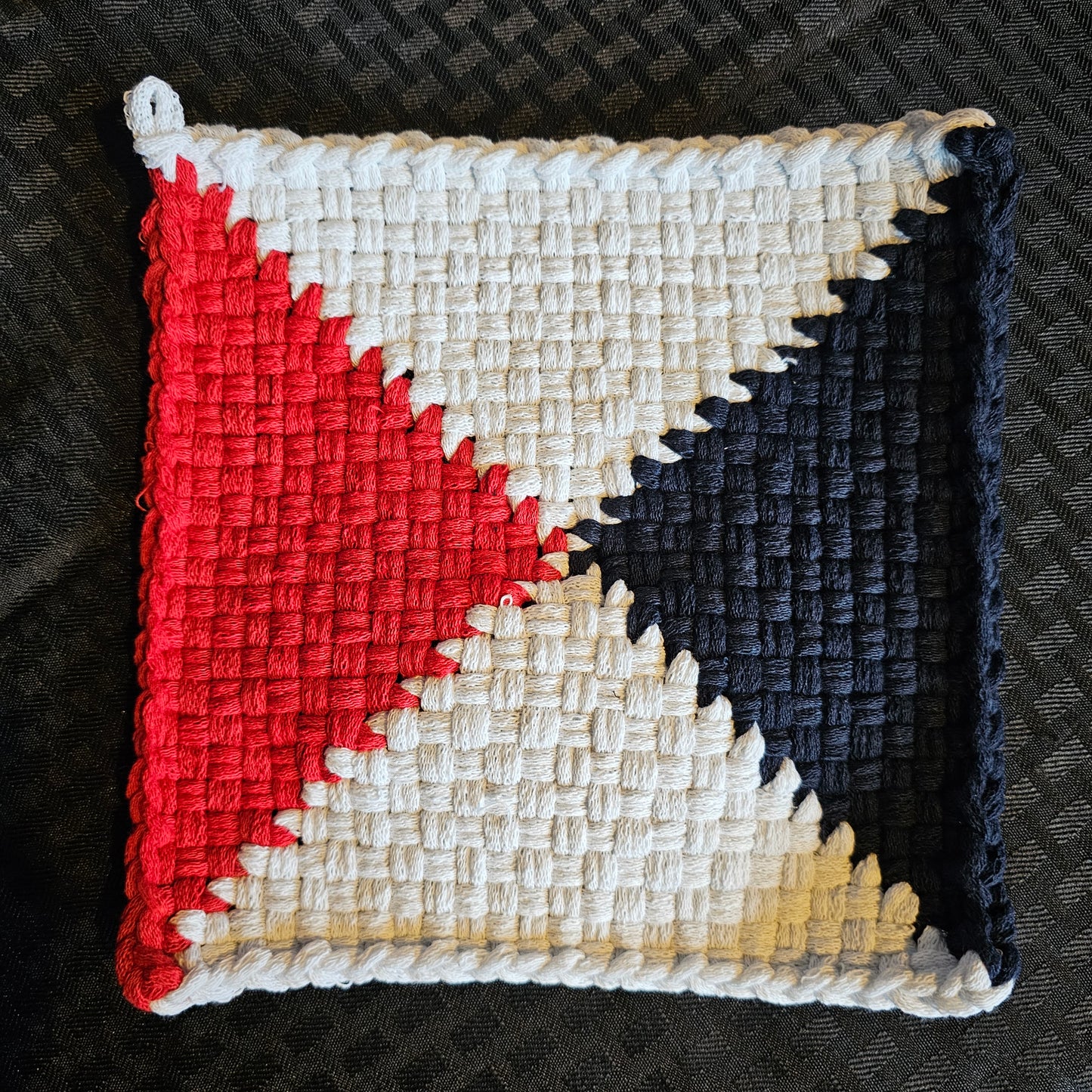 Square woven patch with red, white, and blue geometric pattern on a textured black background