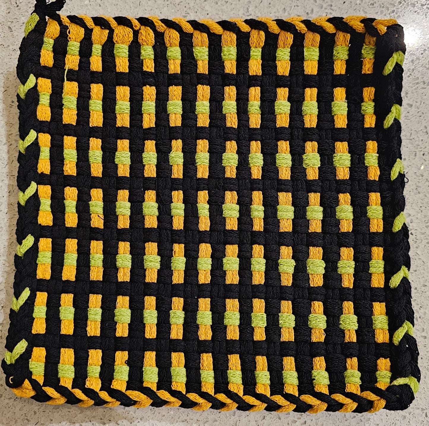 Woven potholder with black, yellow, and green pattern on a neutral background