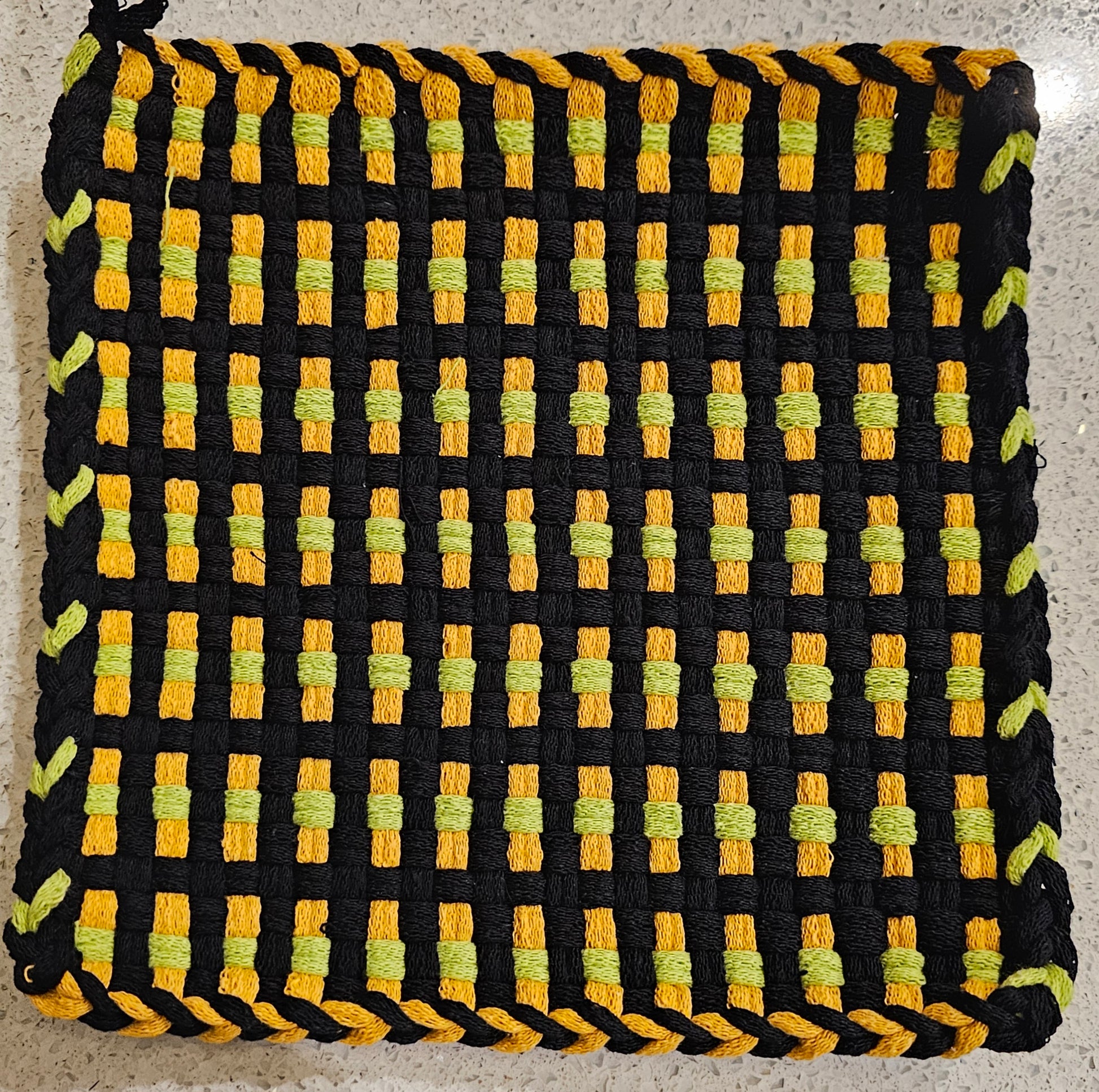 Woven potholder with black, yellow, and green pattern on a neutral background