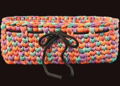 A rectangular crocheted basket made from multicolored t-shirt ribbon in orange, purple, teal, and pink, with a black drawstring tied in the front. Perfect for the TV room or kitchen to catch all those little odds and ends.  11x4x4 inches overall