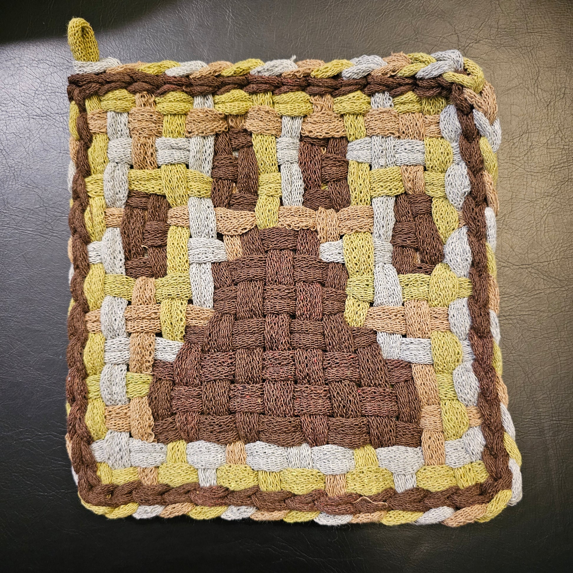 Woven square mat with brown, yellow, and white pattern on a dark background