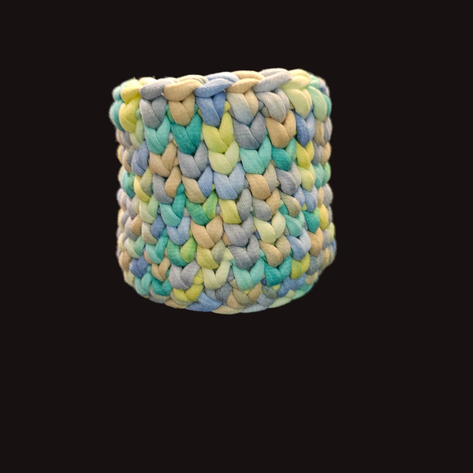 A cylindrical basket made with a chunky crocheted t-shirt cord in pastel shades of blue, green, yellow, and beige. 5x5x5 inches overall. Perfect for pens and pencils or combs and brushes.