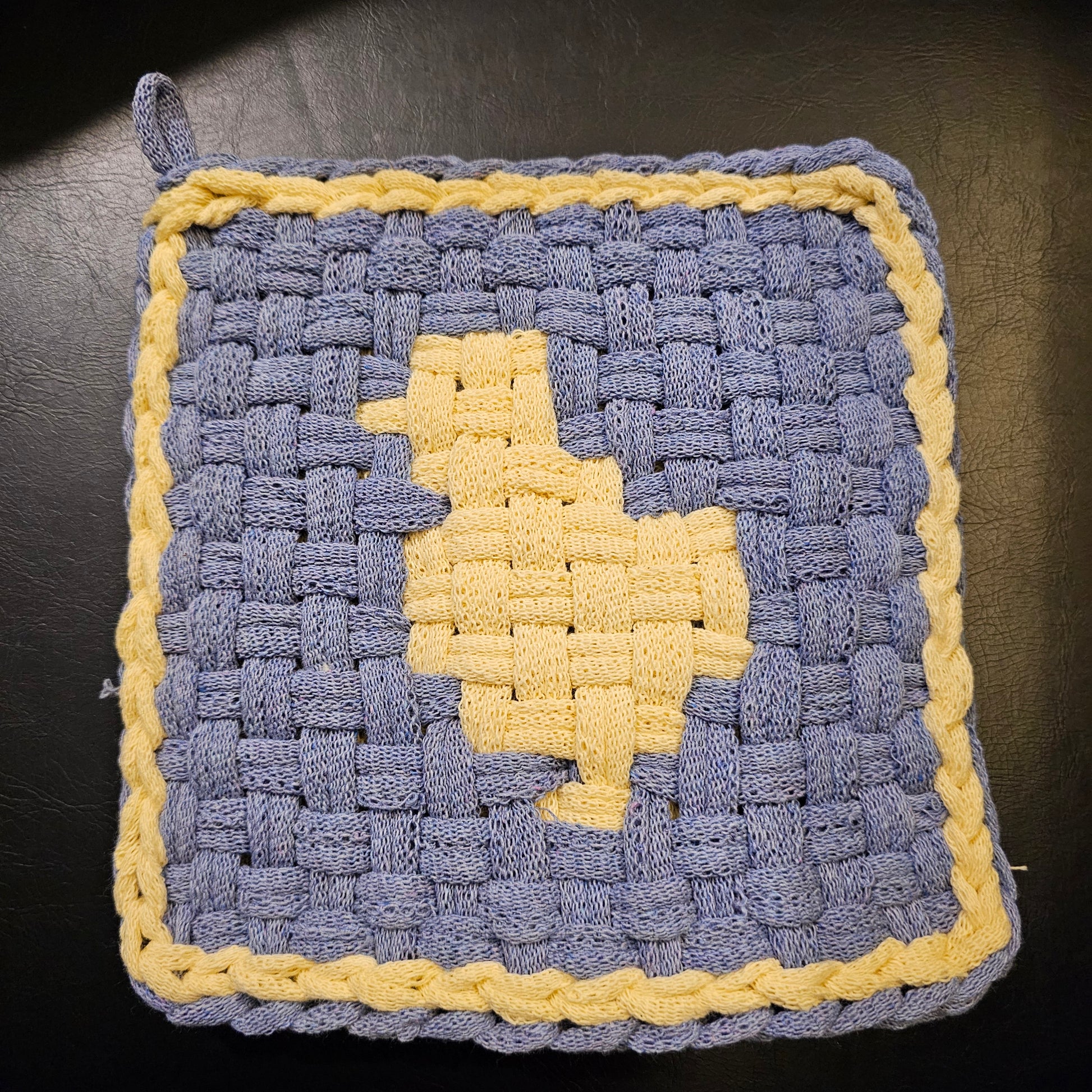 Woven pot holder with blue and yellow pattern on a dark surface