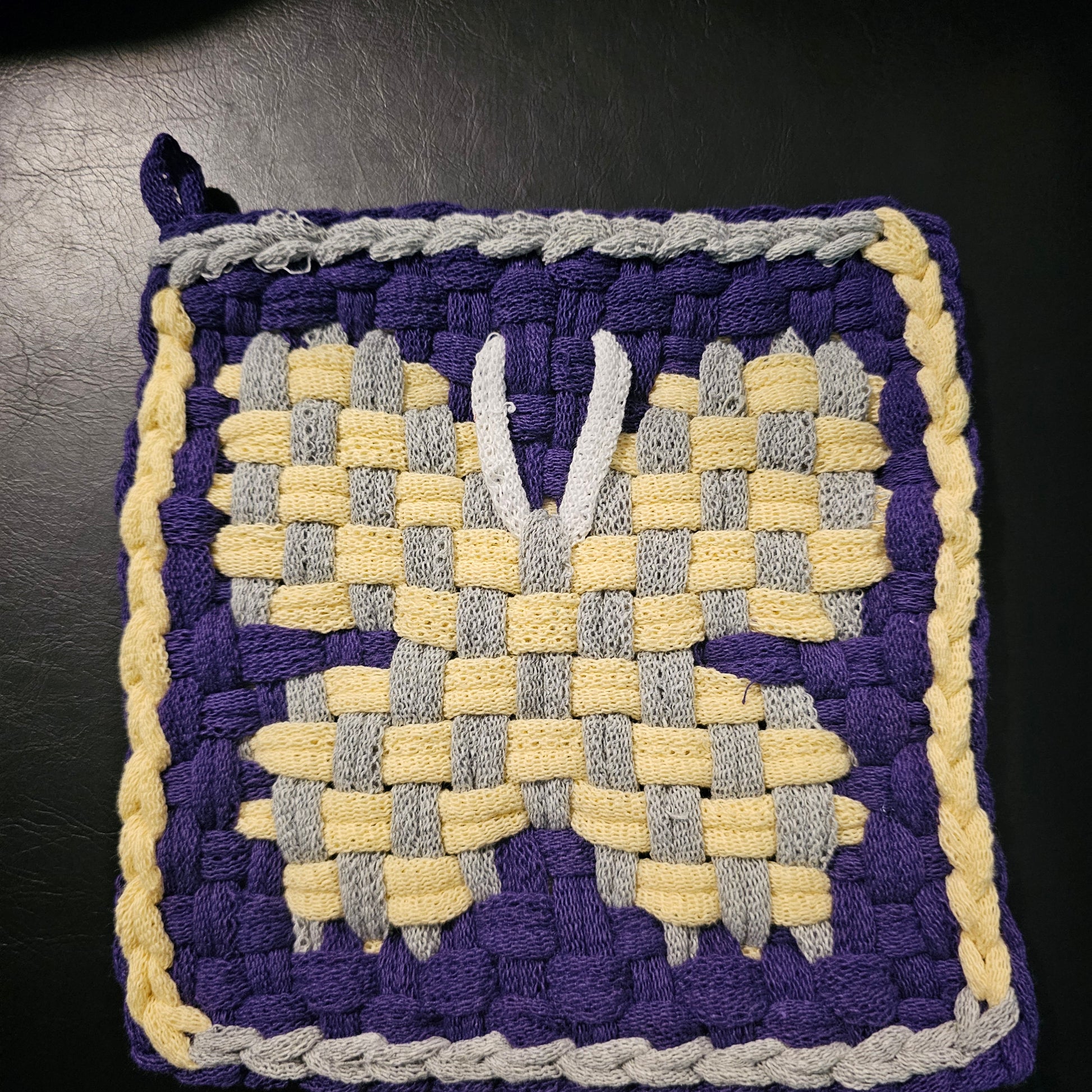 Woven square with purple, yellow, and gray pattern on a dark background