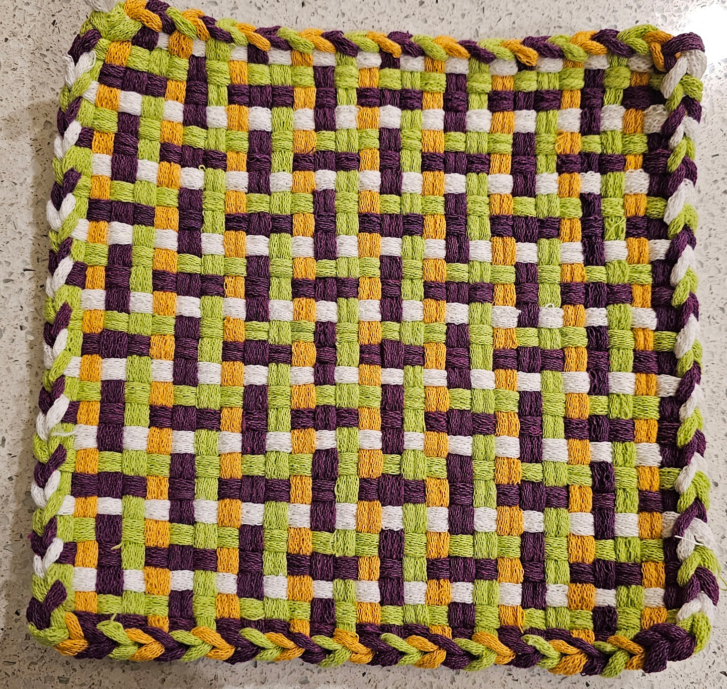 Woven mat with a geometric pattern in green, purple, yellow, and white 