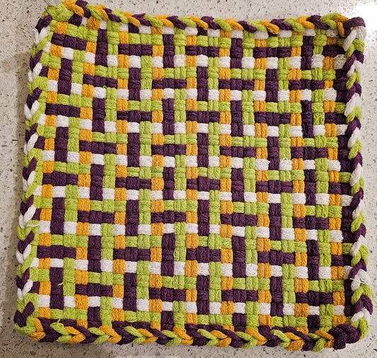 Woven mat with a geometric pattern in green, purple, yellow, and white 