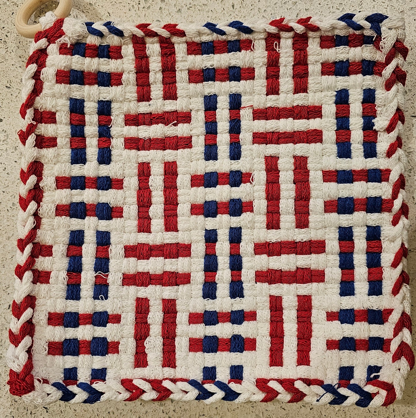 Woven mat with red, white, and blue pattern on a textured surface