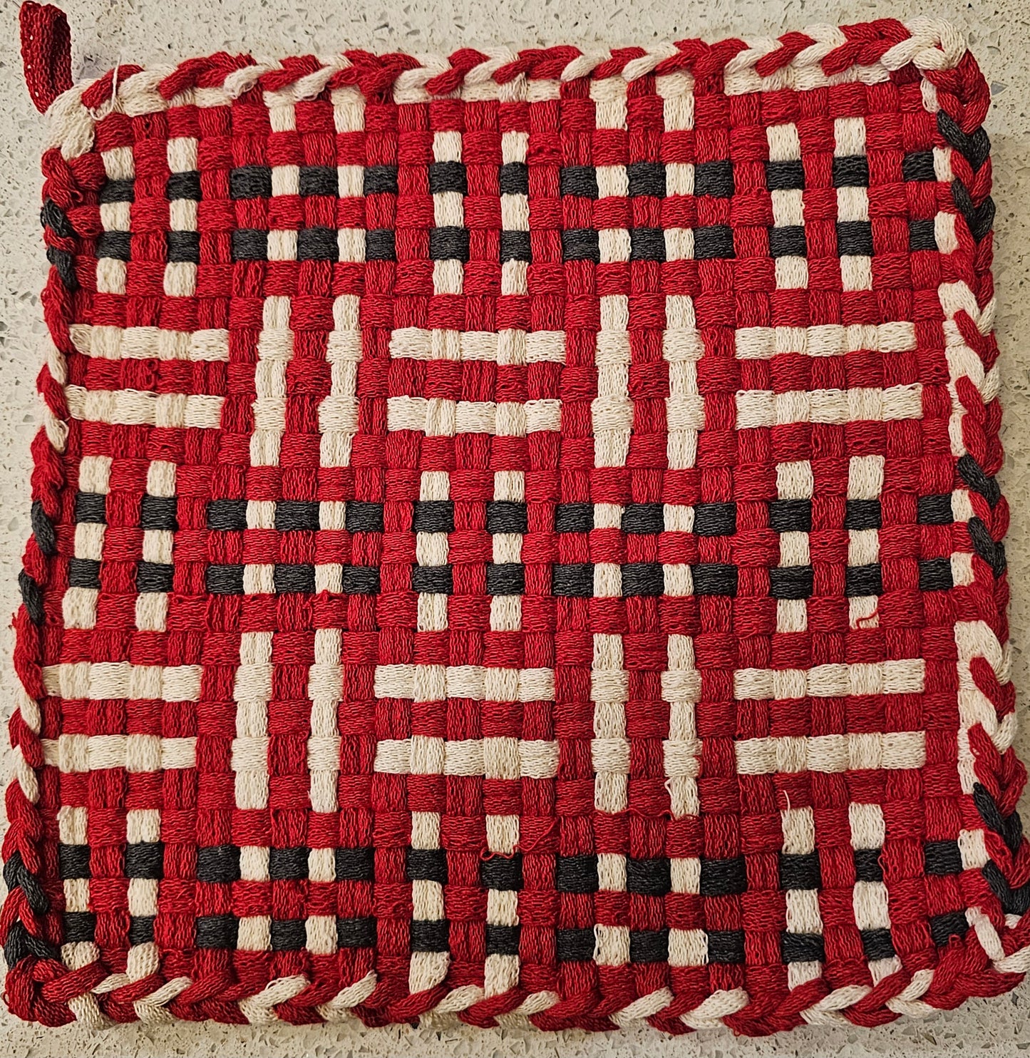 Woven trivet with red, black, and white pattern 