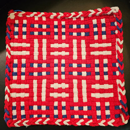 Woven trivet with red, white, and blue pattern on a dark background