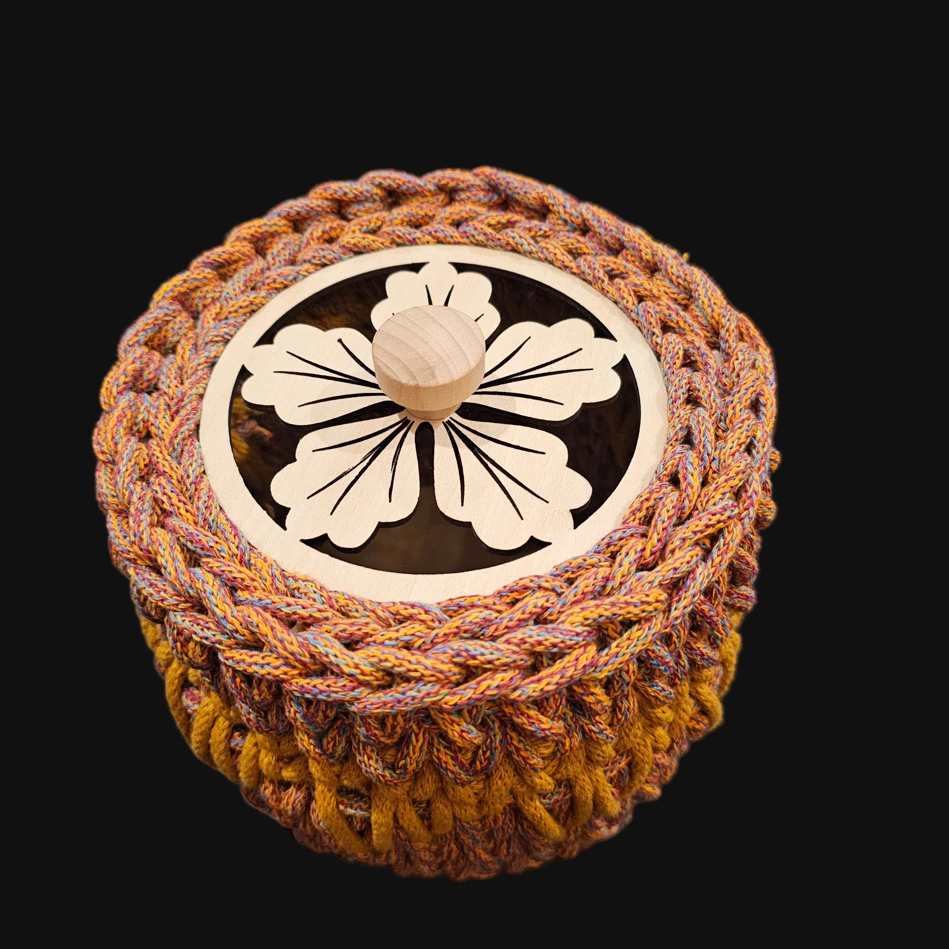 A round crocheted basket in warm brown, beige, and gold tones; featuring a floral cutout lid. 6x6x6 inches overall. Basket opening is 4 inches in diameter.