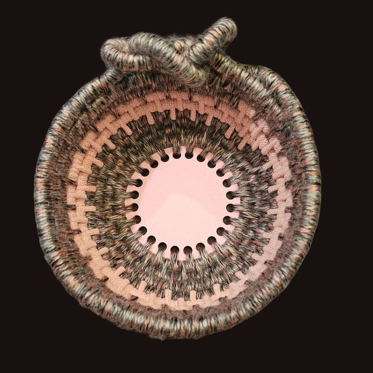 A hand-woven coiled basket with an accent knot, made using variegated gray and pink fuzzy yarn with pink accents