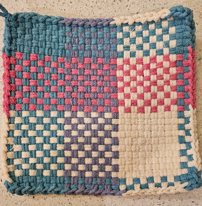 Woven mat with a checkered pattern in blue, pink, and white on a textured surface.