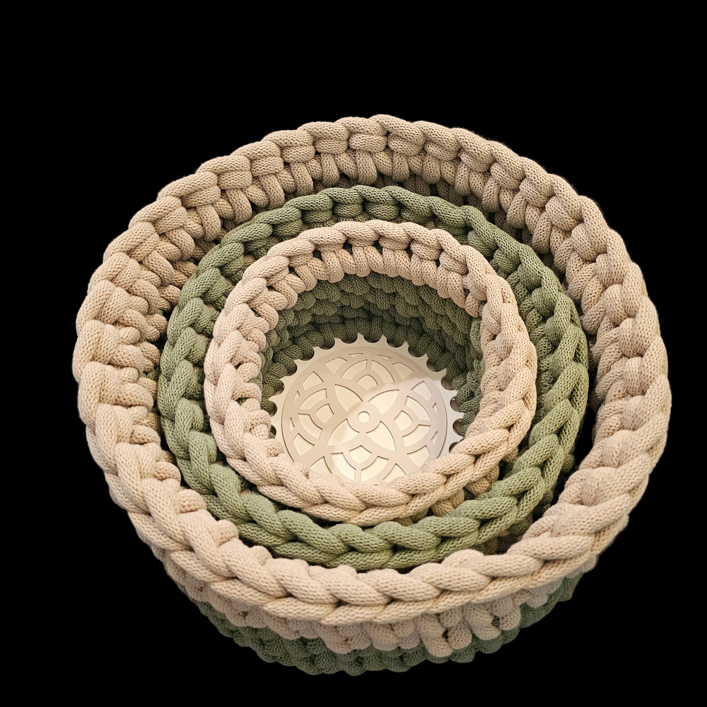 Three nested round woven baskets in natural beige, sage green, and olive green, with the largest basket resting on a black chair.