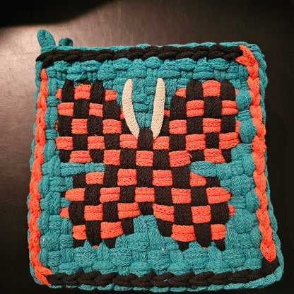 Woven square with a geometric pattern in teal, orange, and black on a dark background