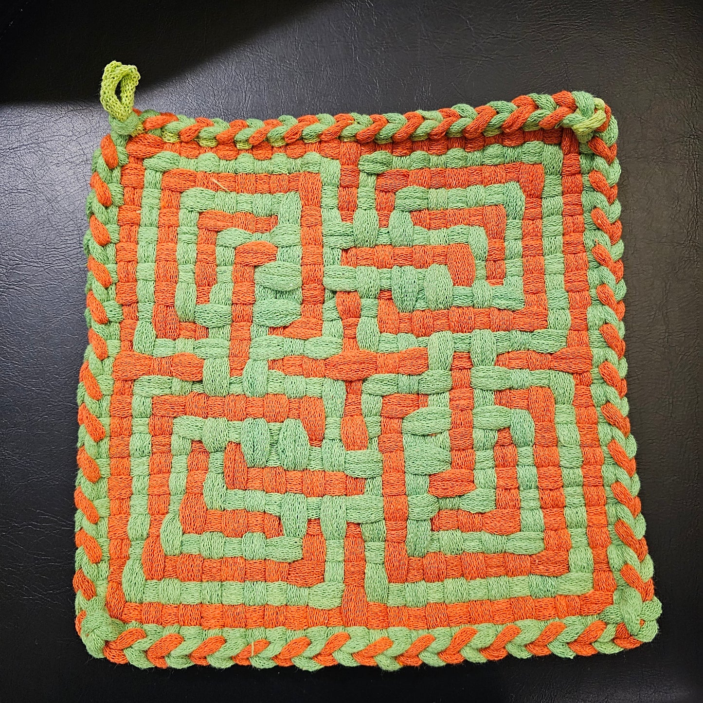 Woven square trivet with orange and green pattern on a dark background