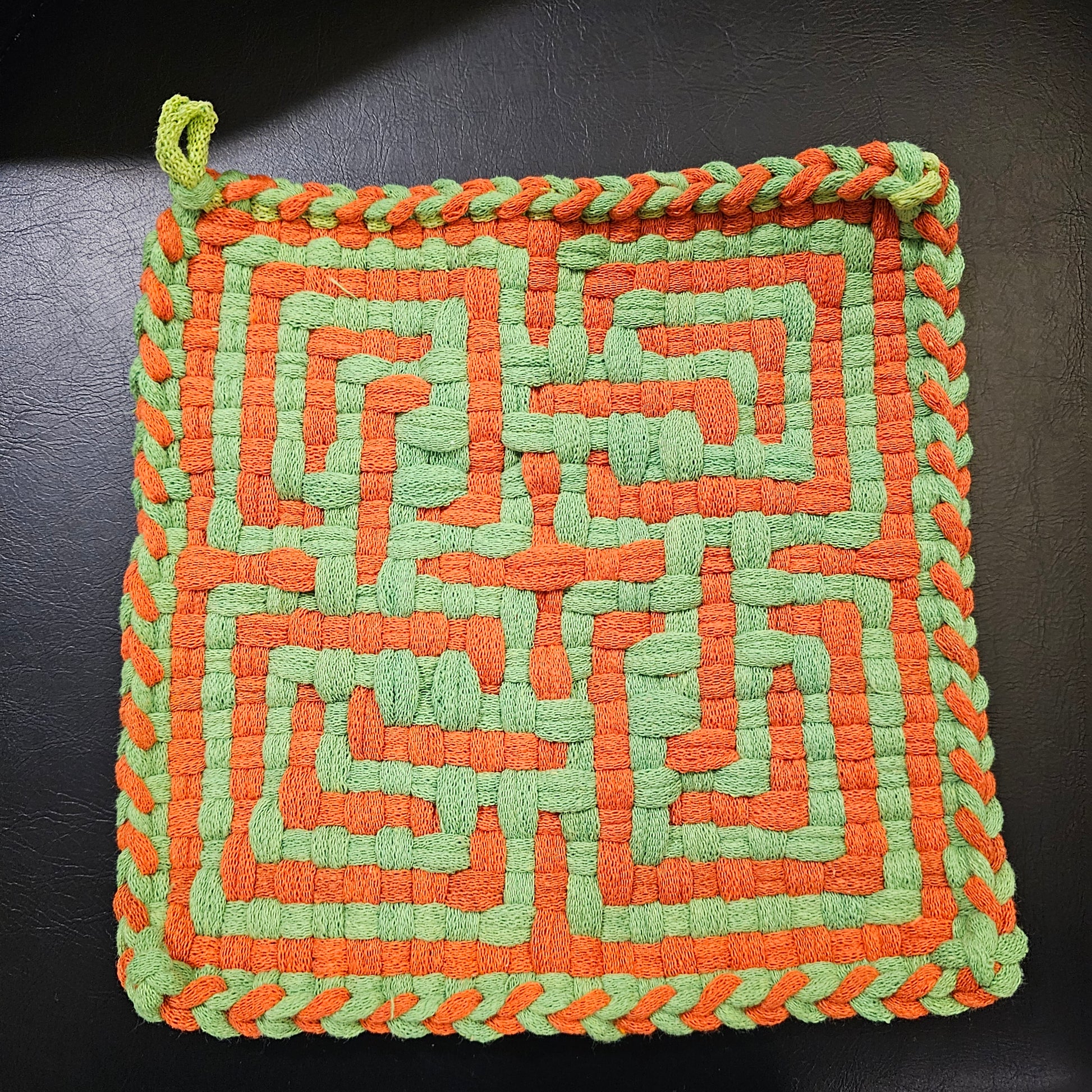 Woven square trivet with orange and green pattern on a dark background