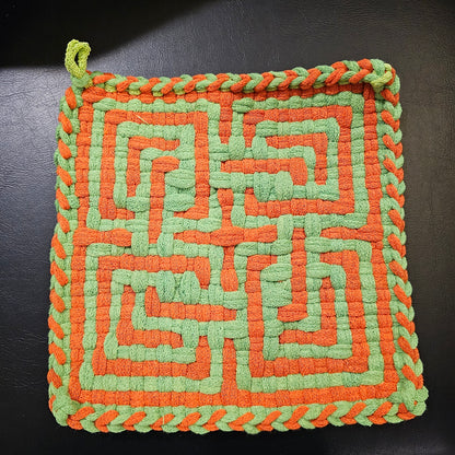 Woven square trivet with orange and green pattern on a dark background