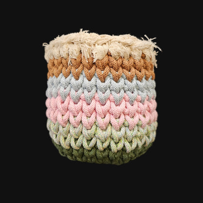 A handmade crocheted basket with a textured chevron pattern, featuring horizontal stripes of cream, brown, light blue, pink, sage green, and olive green, featuring a thick cream-colored frayed outer rim.  5x5x6 inches overall