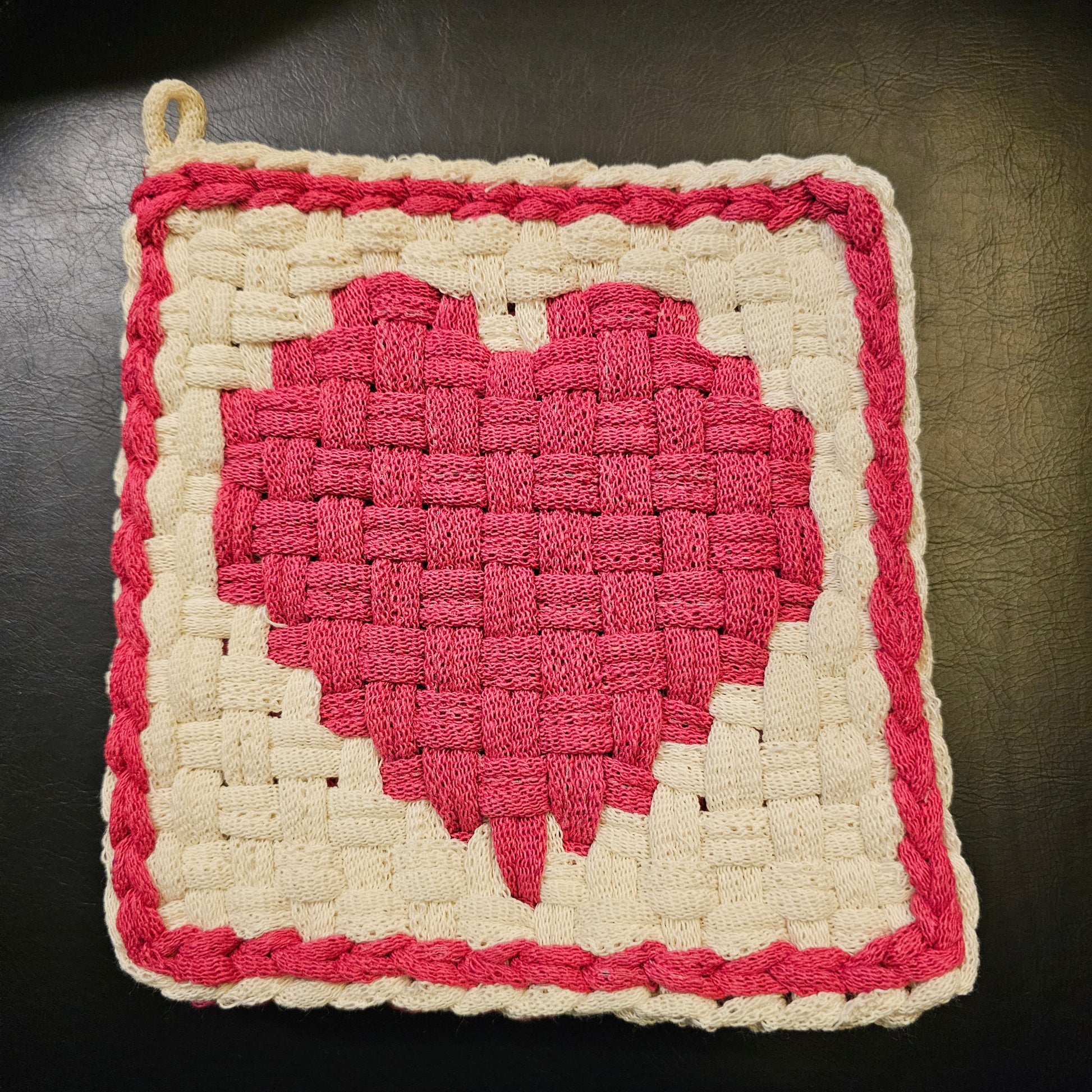 Crocheted square with a pink center and white border on a dark background