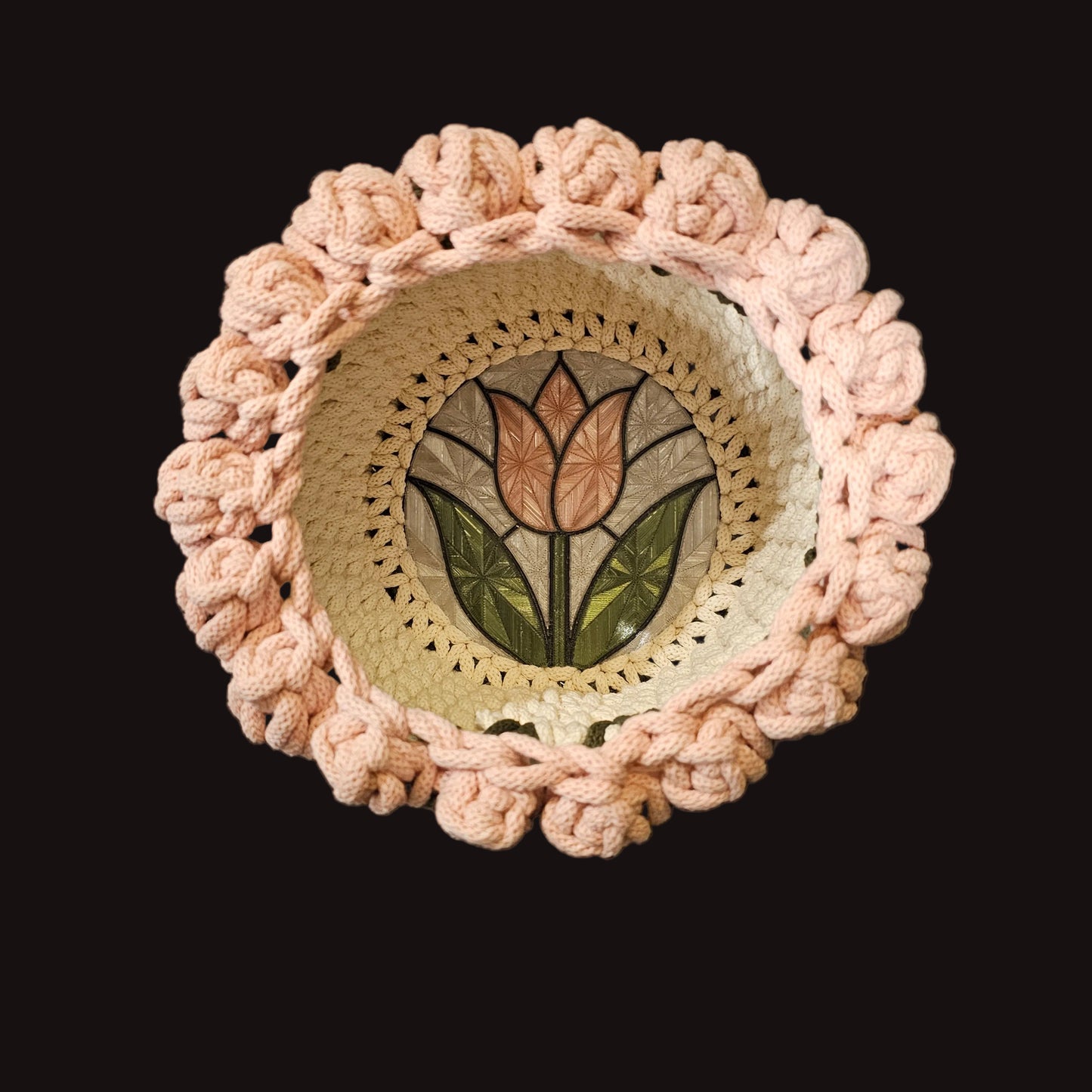 A round crocheted cream basket with a decorative stained glass tulip design in the center, surrounded by a chunky crocheted light pink border, resembling tulips. 8x8x6 inches overall