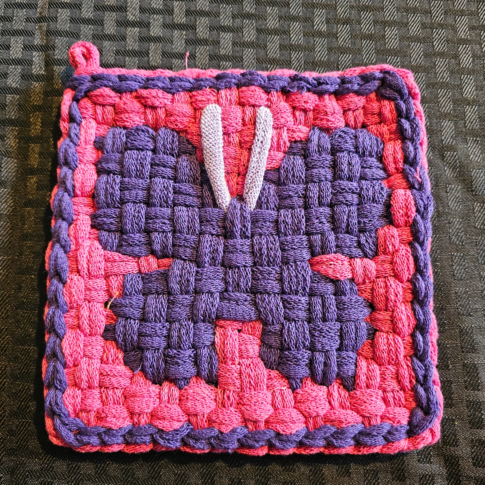 Woven square patch with pink and purple pattern on a textured surface