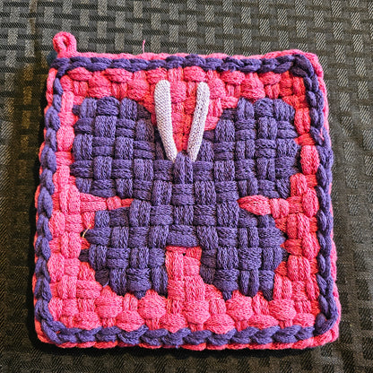 Woven square patch with pink and purple pattern on a textured surface