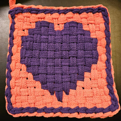 Hand-woven square mat with purple center and pink border on a dark background