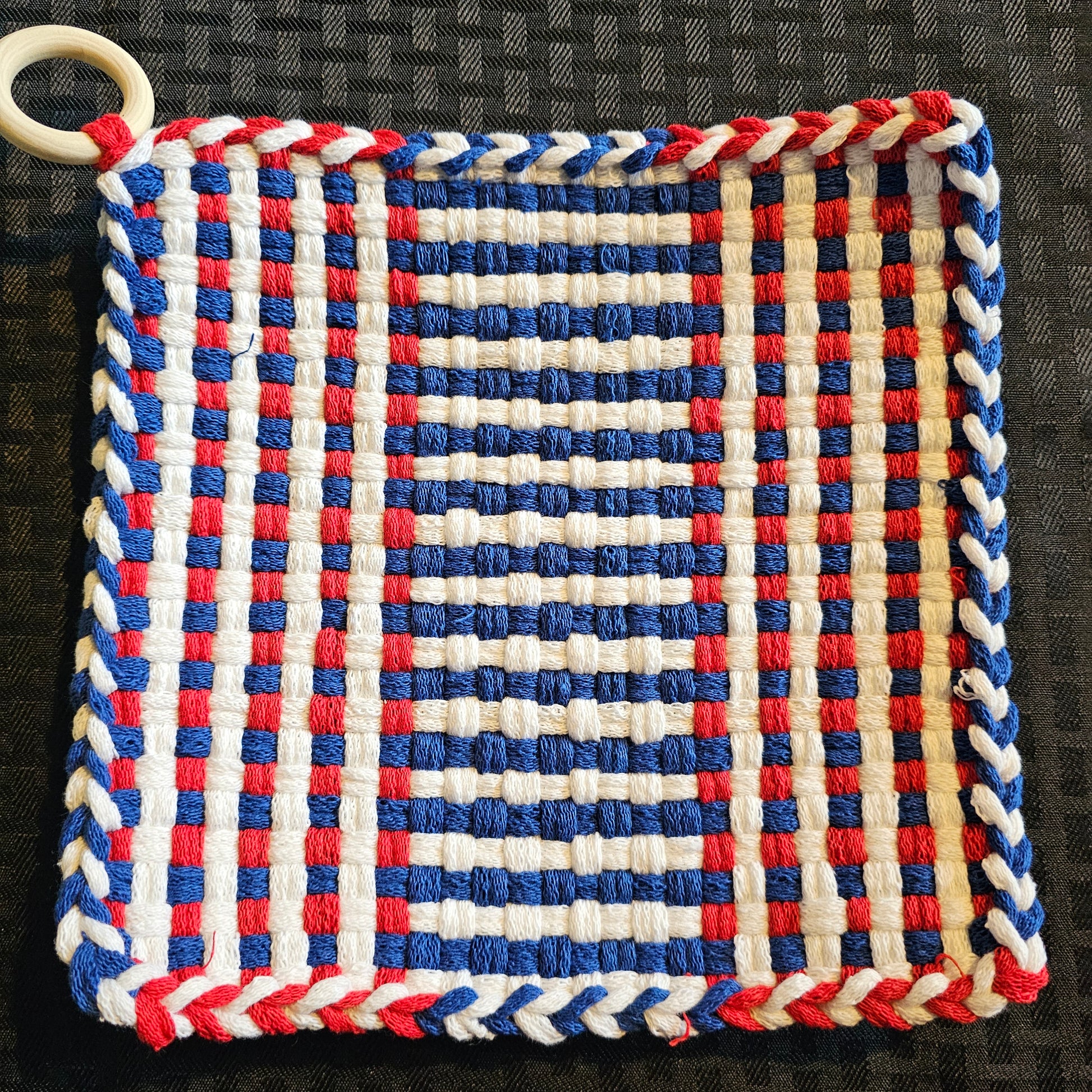 Woven trivet with red, white, and blue pattern on a black background