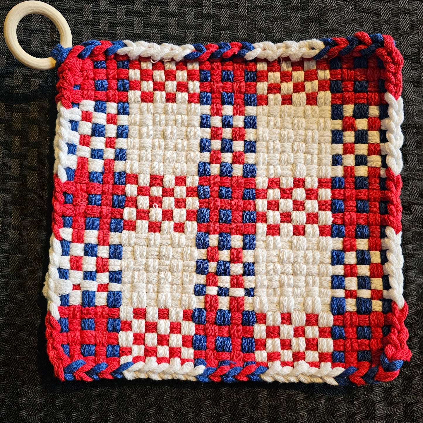 Woven square with red, white, and blue pattern on a textured black background