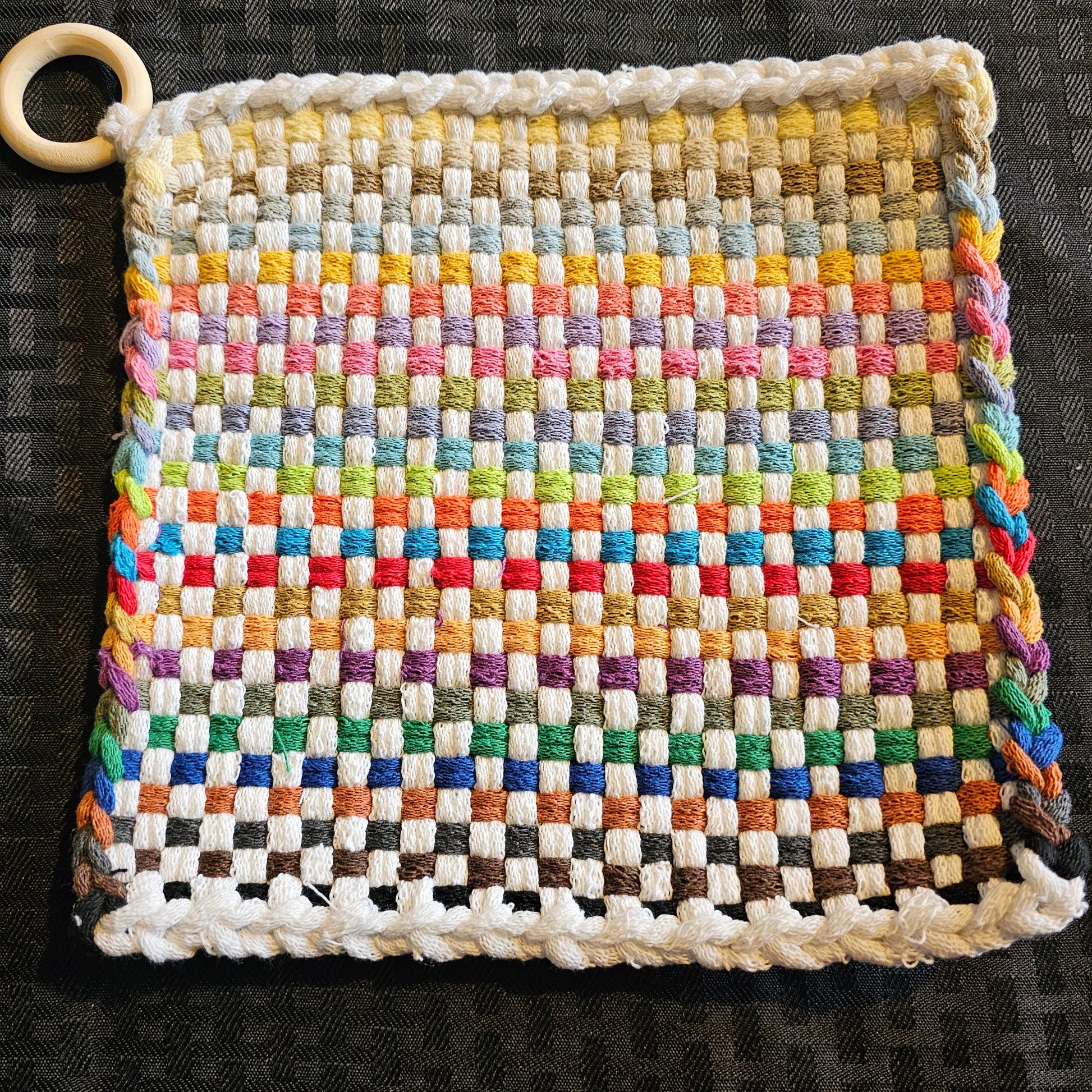Multicolored woven potholder with a wooden ring on a dark background
