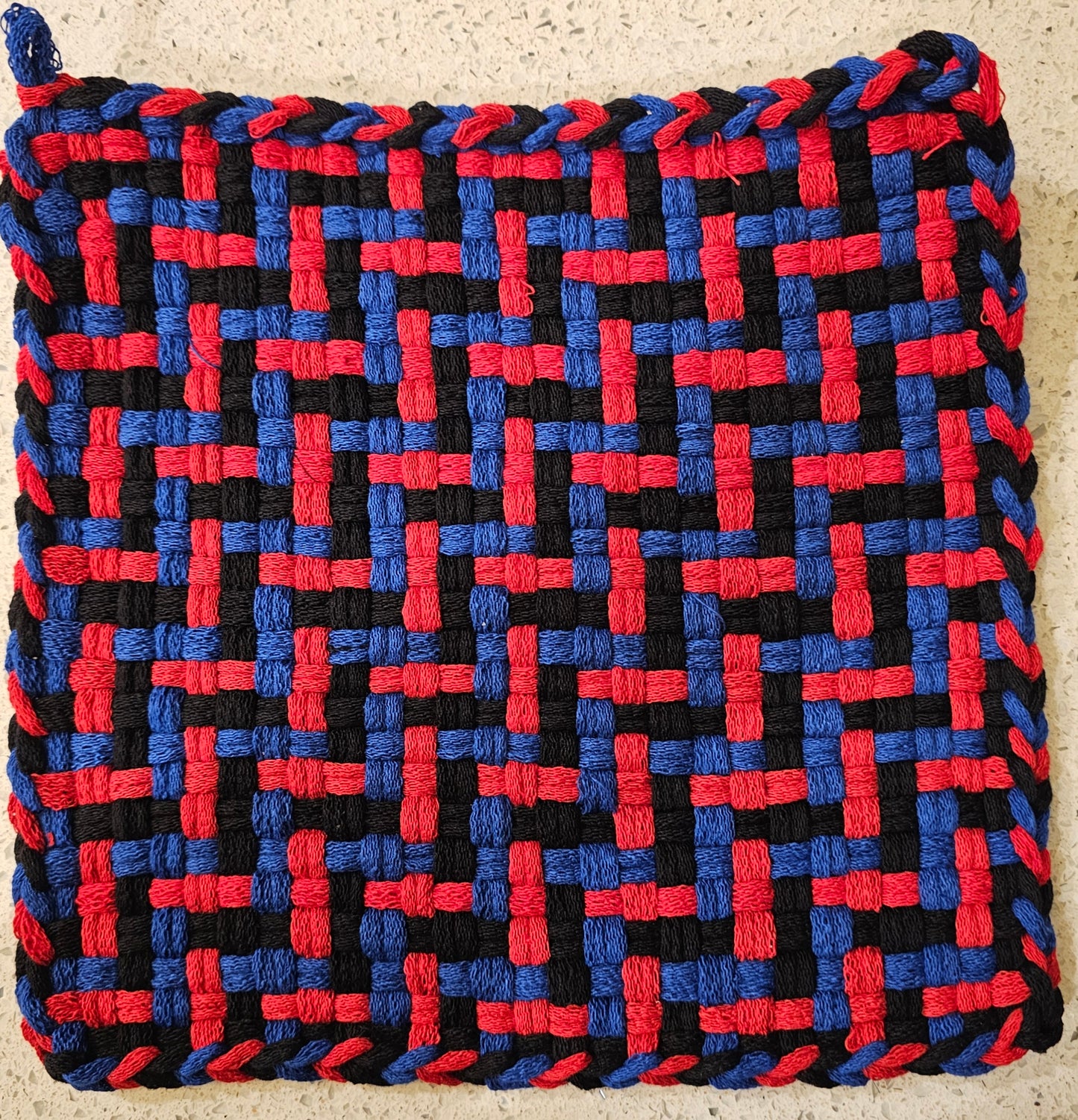 Woven trivet with red, blue, and black pattern on a beige surface