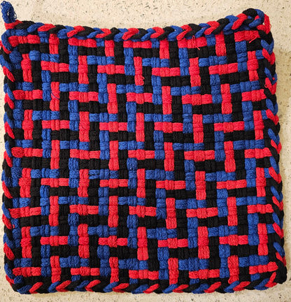 Woven trivet with red, blue, and black pattern on a beige surface