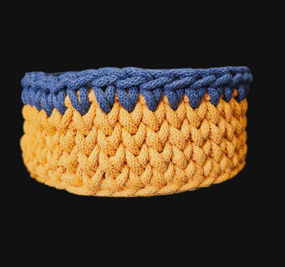 A round crocheted basket with an octopus design, featuring navy blue outer crochet trim, an orange middle band, and a dark blue center with a yellow-orange octopus and green seaweed pattern. 6x6x3 inches overall