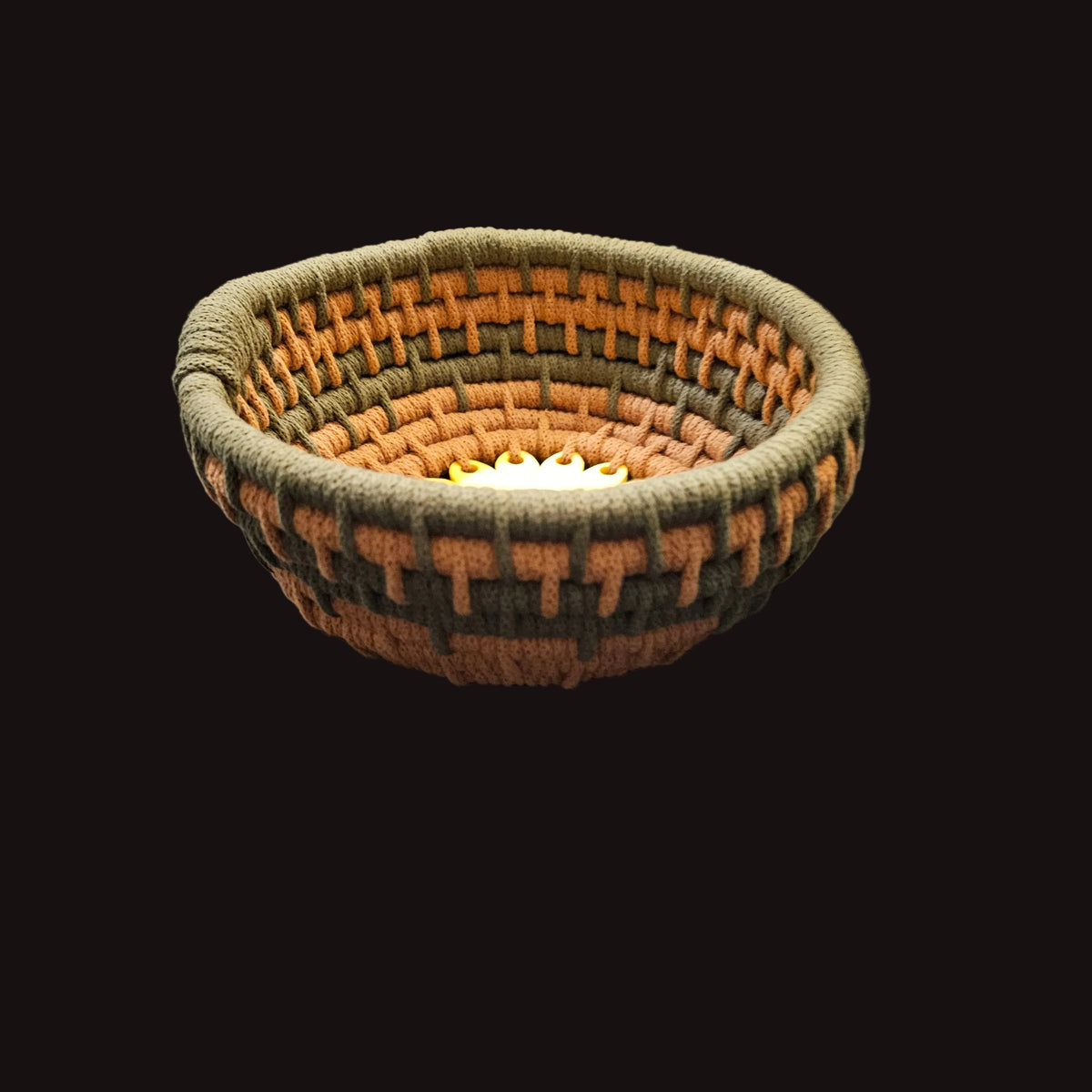A handwoven basket with concentric rings of olive green, terracotta, and brown yarn, featuring a sunflower design in the center. 