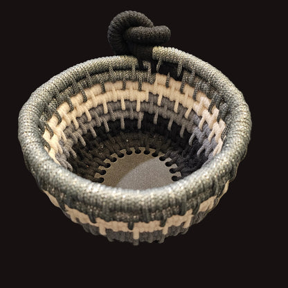 A small woven basket with a loop handle, featuring a black, gray, and cream striped pattern with silver sparkles...shining bright.