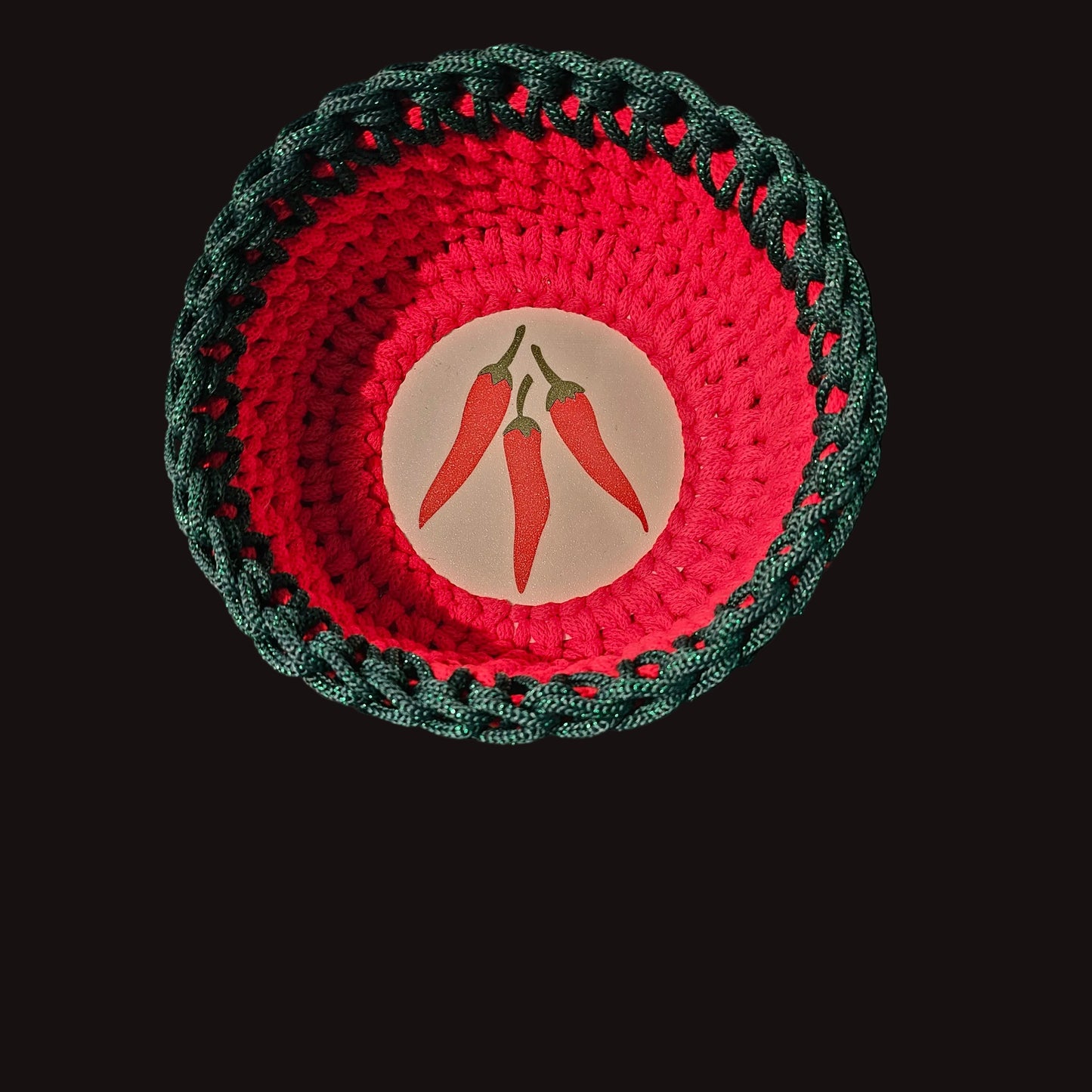 A handmade crocheted bowl using red and sparkly deep green cord, featuring three red chili peppers.  7x7x3 inches overall