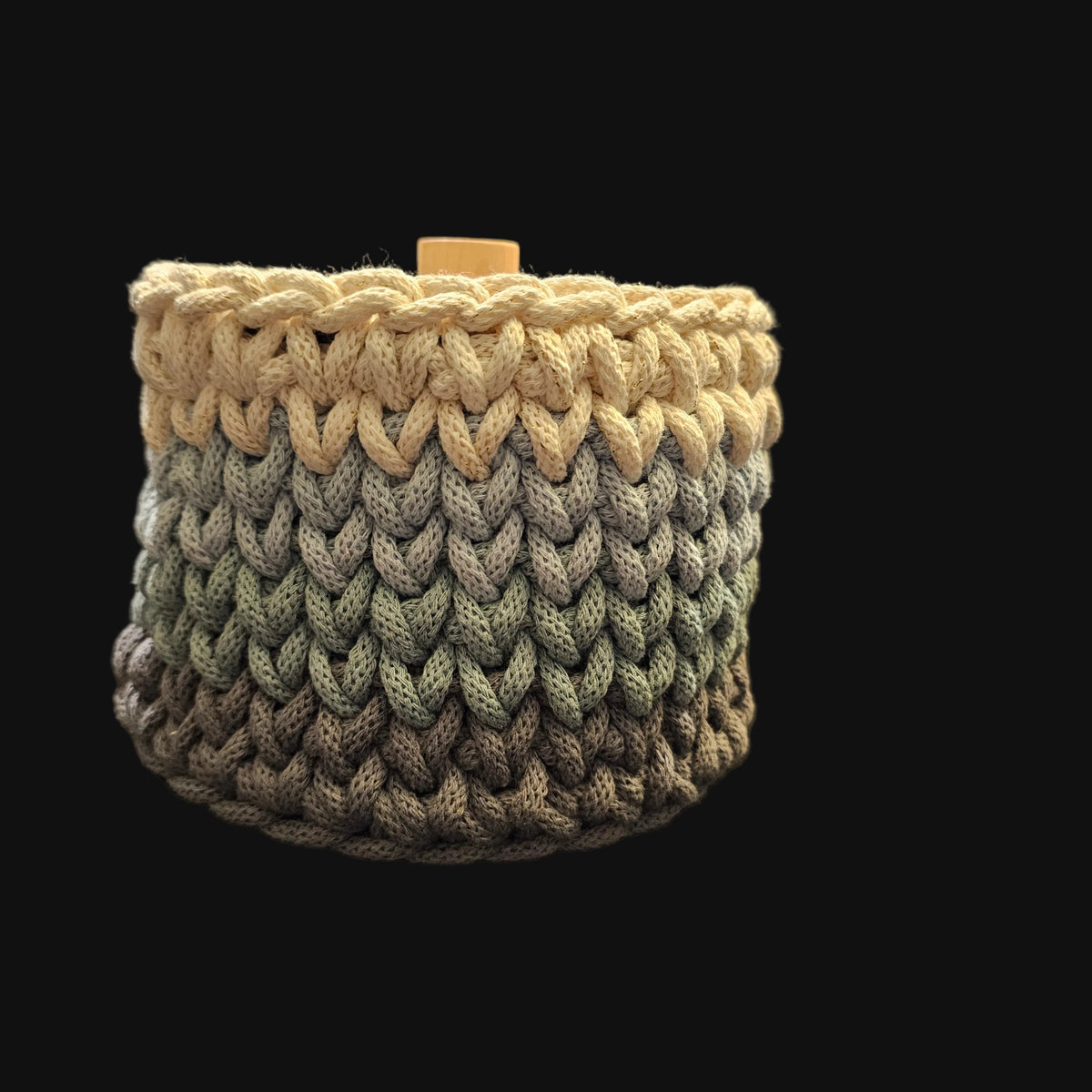 A round crocheted basket in cream (with flecks of gold thread), light blue, and gray with a matching round wooden lid featuring an engraved floral wreath design and a small wooden knob. 6x6x5 inches overall; basket opening is 4 inches in diameter.