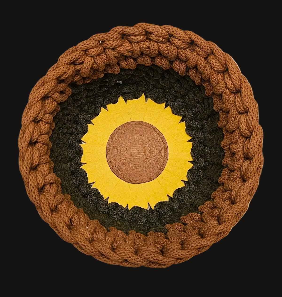 A crocheted basket with a bright yellow sunflower at its center. This basket is a two-tone design, featuring a warm brown top section and an olive-green bottom section. 7x7x4 inches overall
