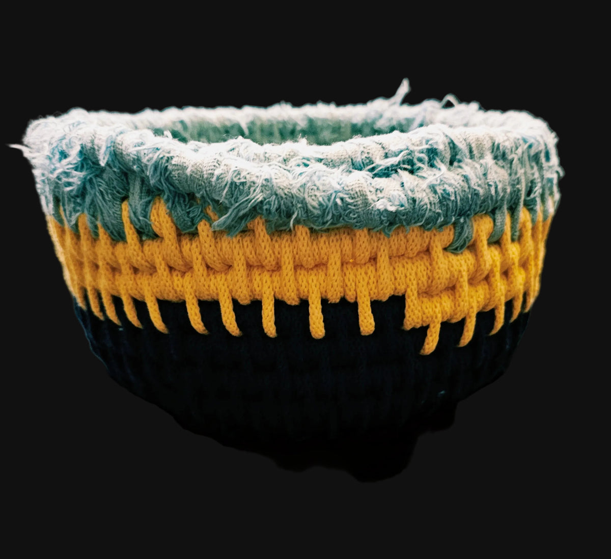 A circular coiled basket with a rustic frayed outer edge, featuring concentric rings of light blue, yellow, and dark navy over a central printed illustration of a tulip field at sunset. 9x9x4 inches overall