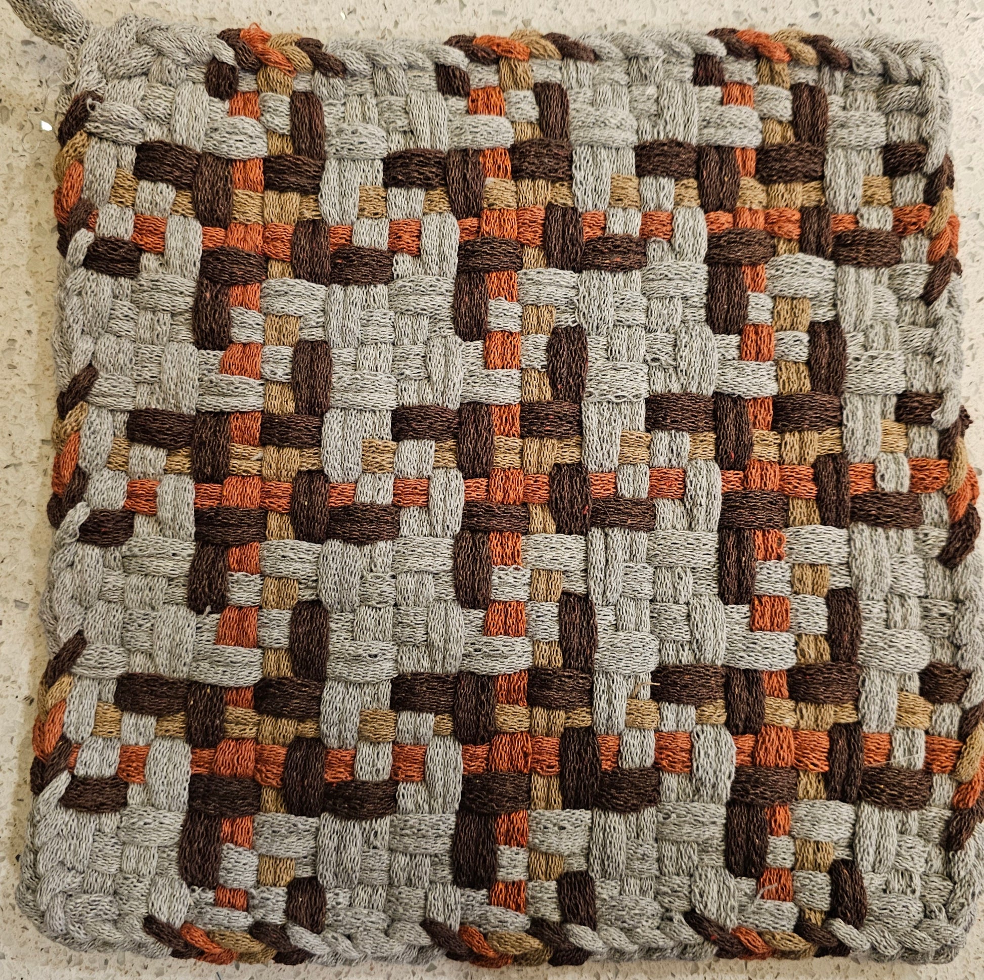 Woven potholder with a geometric pattern in earthy tones 
