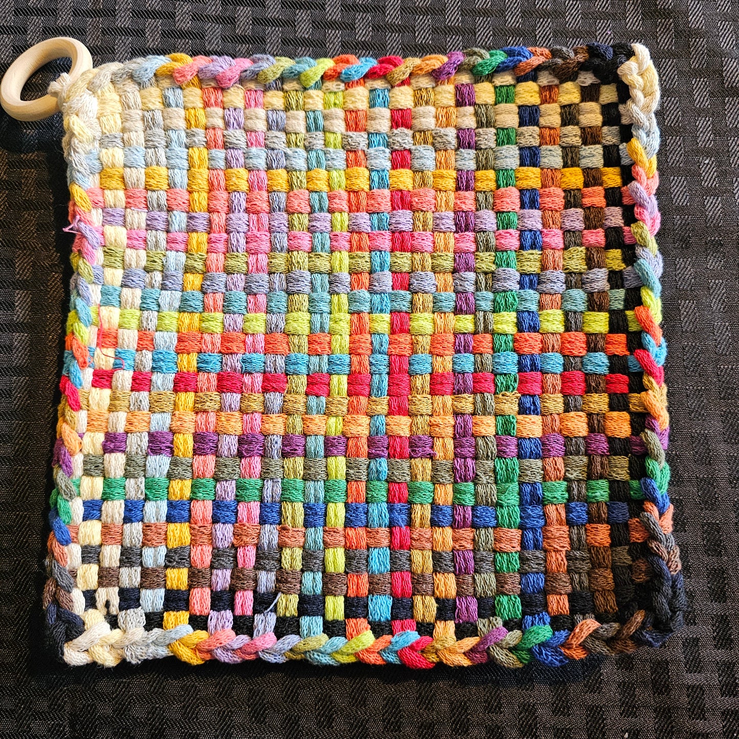 Multicolored woven potholder with a handle on a dark textured background