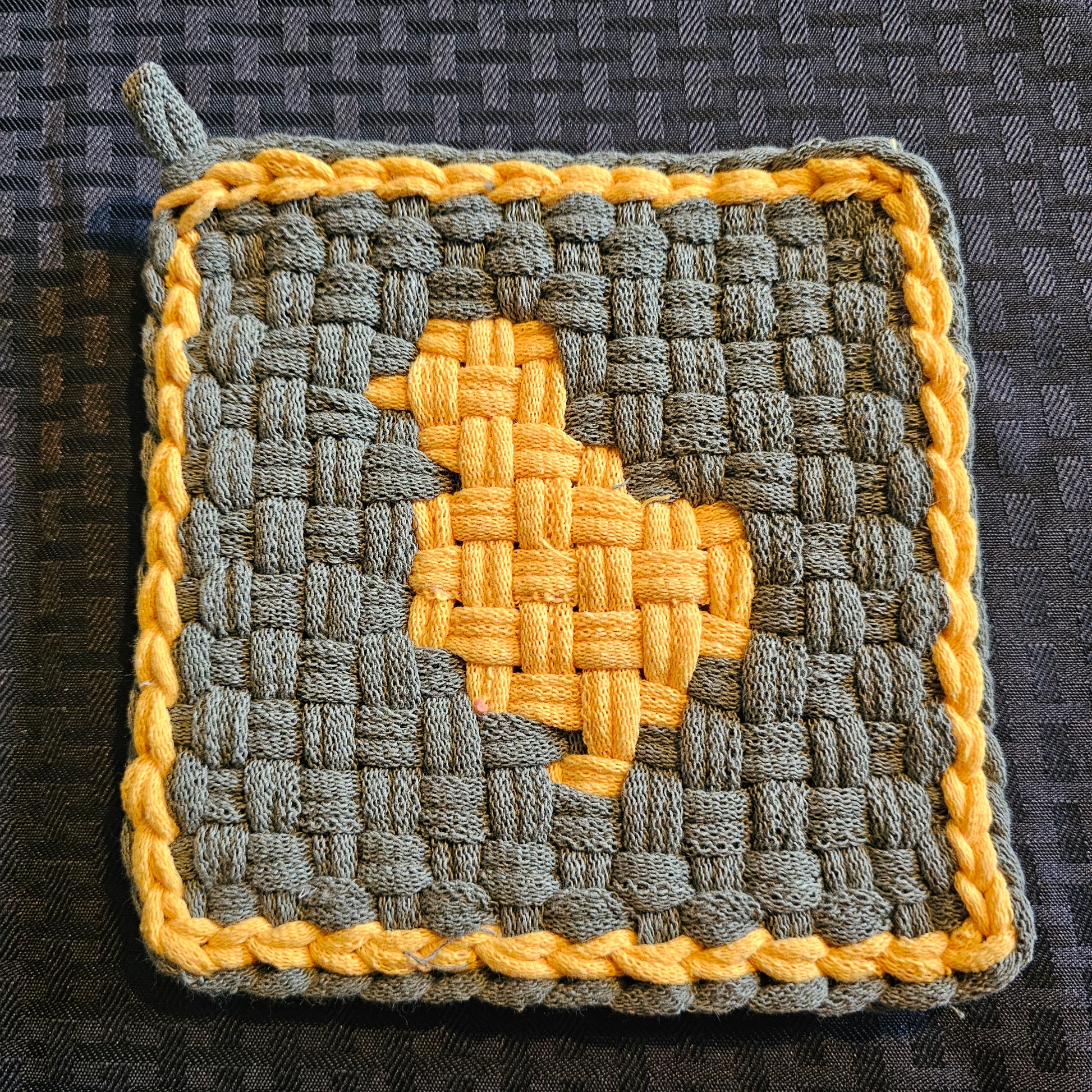Gray and yellow woven potholder with a star design on a textured surface