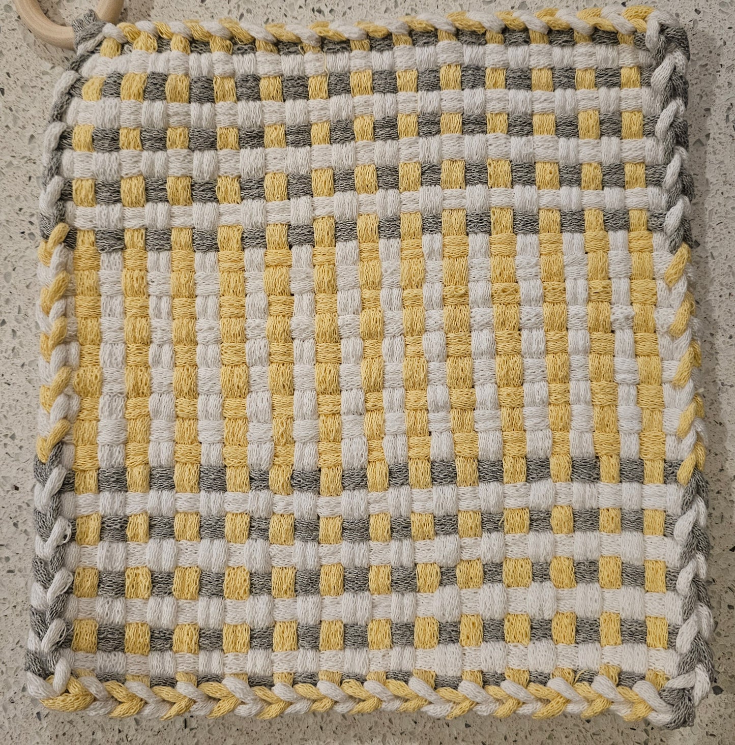 Woven fabric square with yellow, gray, and white pattern on a concrete surface