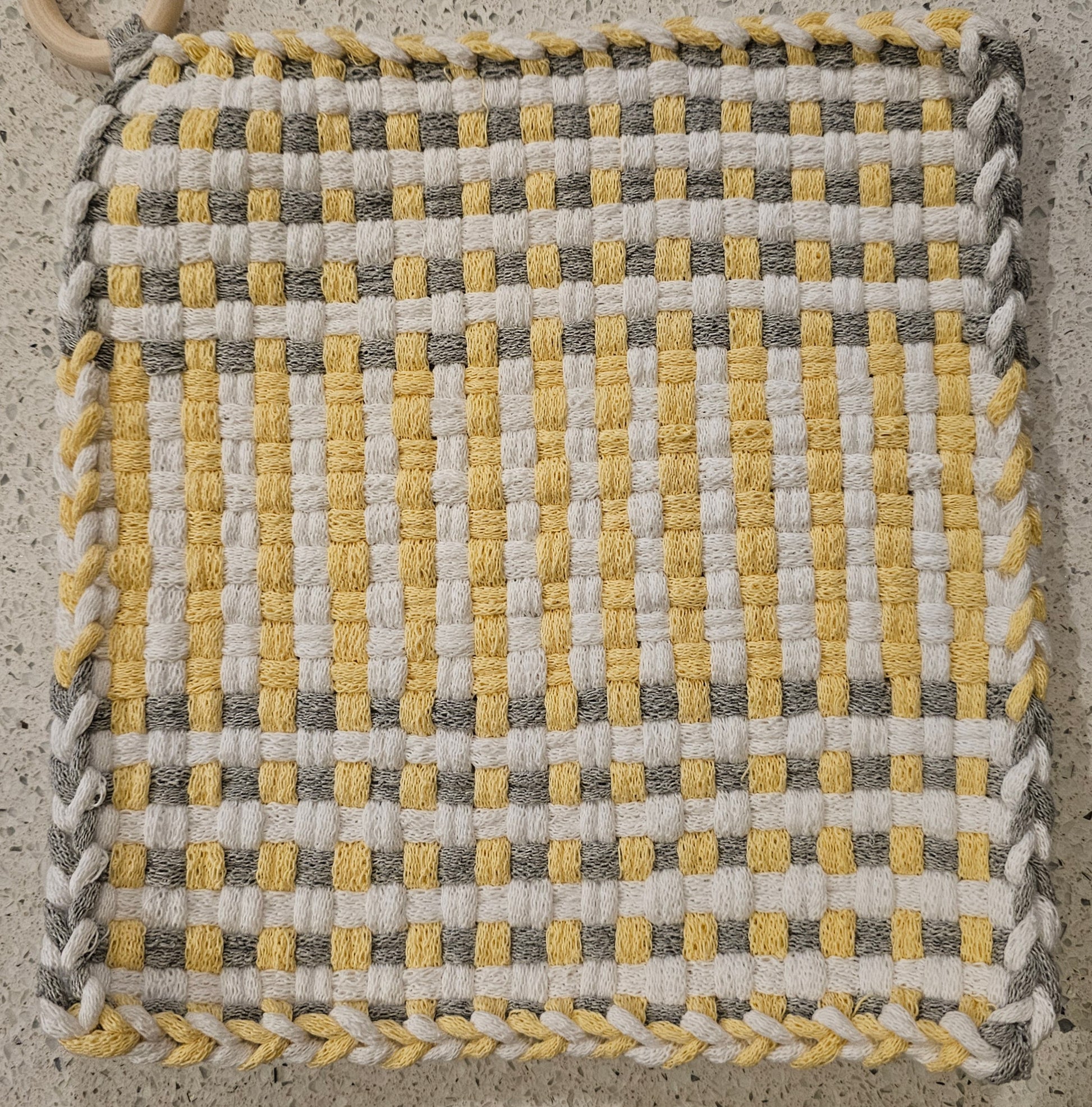 Woven fabric square with yellow, gray, and white pattern on a concrete surface