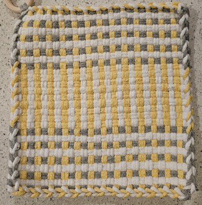 Woven fabric square with yellow, gray, and white pattern on a concrete surface