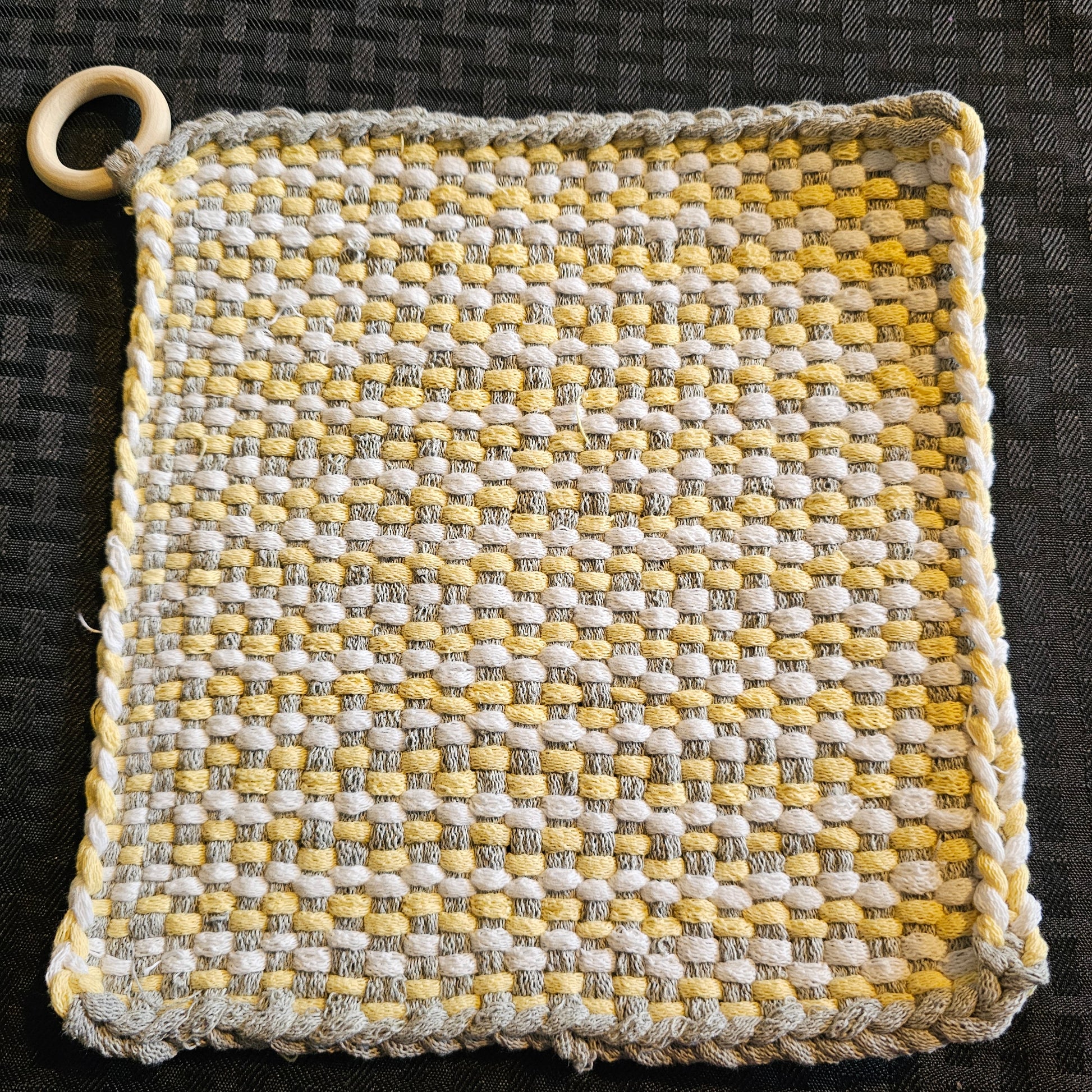 Woven potholder with yellow, gray, and white pattern on a black background